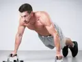 Mężczyzna wykonuje pompki na uchwytach. Pompki wzmacniają klatkę piersiową, ramiona i brzuch, budując siłę i wytrzymałość.