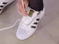Pokazuję, jak wiązać sznurówki w adidasach Superstar. Białe sznurówki przeplatane przez czarne paski.