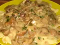 Makaron farfalle z kremowym sosem z maślaków i posiekaną natką pietruszki na żółtym talerzu.