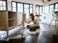 Mujer lijando muebles de madera antiguos para restaurarlos.