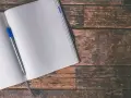 Otwarty notatnik z niebieskim długopisem na drewnianym stole. Czekam na inspirację, by stworzyć koło kwintowe.