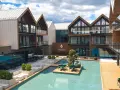Nowoczesny hotel z basenem i tarasami. W centralnym punkcie basen z wyspą i stolikami, otoczony budynkami z drewnianymi elementami. Idealne miejsce na wypoczynek, jak w bajkowym jagniątkowie.