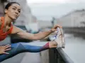 Kobieta w sportowym stroju rozciąga nogę, przygotowując się do treningu cardio nad kanałem.
