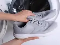 Ręce wkładają szare adidasy do pralki. Dowiedz się, jak prać adidasy w pralce, aby odświeżyć swoje ulubione buty.