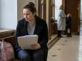 Oskarżona w procesie sądowym, zamyślona, trzyma dokumenty. Obok niej plecak i kurtka.