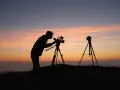 Sylwetka fotografa z kamerą na statywie o zachodzie słońca. Zastanawiasz się, ile zarabia fotograf miesięcznie?