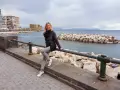 Woman sitting on a railing with Castel dell'Ovo and the sea in the background in Naples.