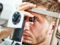 Mężczyzna podczas badania okulistycznego. Lekarz używa urządzenia do angiografii fluoresceinowej, aby zbadać jego oko.