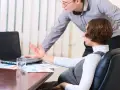 Kobieta w ciąży dyskutuje z kolegą o umowie na zastępstwo, analizując dokumenty przy laptopie.