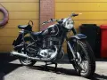 Klasyczny czarny motocykl, model iż 49, lśni w słońcu. Obok żółta brama i ceglana ściana.