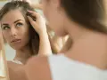 Besorgte Frau prüft im Spiegel ihr Haar, möglicherweise wegen Haarausfall in der Schwangerschaft.