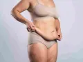 Kobieta w bieliźnie pokazuje fałdy brzuszne, rozważając abdominoplastykę.