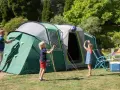 Radosny camping rodzinny: tata rozkłada namiot, dzieci bawią się piłką, mama przygotowuje posiłek.