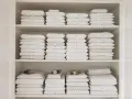 Étagères remplies de linge de lit blanc et beige plié. Une astuce rangement linge de lit pour une organisation parfaite.