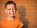 Uśmiechnięty chłopiec w pomarańczowej koszulce. Dziecko mówi o sobie w 3 osobie: "On jest szczęśliwy!".