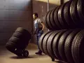 Un operaio trasporta pneumatici su un carrello, pronto per la manutenzione pneumatici. Scaffali pieni di gomme sullo sfondo.