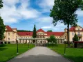 Eleganckie, żółte budynki z czerwonymi dachami, przypominające stare łazienki Krynica Zdrój, otoczone zielonym ogrodem.