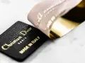 Etichetta in pelle nera con logo Christian Dior Paris e "Made in Italy" dorato, accanto a un nastro Dior francese con finitura oro lucido.