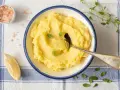 Un cremoso puré de patata de la abuela, servido en un cuenco azul, con una cuchara, limón y sal rosa.