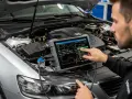 Mechanik diagnozuje problem z samochodem, używając testera do sprawdzenia ECU. Na ekranie widać wykresy parametrów silnika.