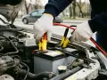 Person mit Handschuhen schließt Starthilfe-Kabel an Autobatterie an. ADAC-Hilfe ist oft die Lösung bei Pannen.