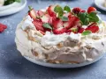 Pyszny tort bezowy z mascarpone i bitą śmietaną, ozdobiony świeżymi truskawkami i miętą.