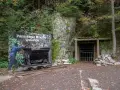 Wejście do Podziemnego Miasta Osówka, z wagonikiem i tablicą informacyjną. Widać skalne ściany i wejście do tunelu.