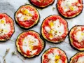 Deliziose pizzette di melanzane con pomodoro e mozzarella filante, condite con olio e erbe aromatiche.