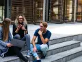 Trójka studentów, w tym jedna osoba na studiach lingwistycznych, siedzi na schodach, korzystając z laptopa i telefonu.