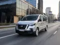 Srebrny van Nissan, jeden z najnowszych nissan modele, jedzie ulicą w nowoczesnym mieście.