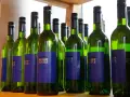 Rząd zielonych butelek białego wina Obsthof Hertle. Lepiej pić drinki czy białe wino? Wybór należy do Ciebie!