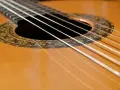 Zbliżenie na gitarę klasyczną. Sześć białych strun biegnie nad ozdobną rozetą.
