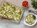 Delicioso calabacín al horno, gratinado y espolvoreado con perejil fresco. Servido en una fuente de vidrio y un plato blanco.