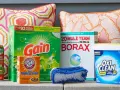 Supplies for how to clean outdoor cushions: Scotchgard, Gain detergent, Borax, baking soda, OxiClean, and a scrub brush.