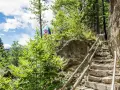 Ein Paar genießt die Aussicht vom Schenner Waalweg. Steintreppen führen durch üppige Vegetation und Felsen.