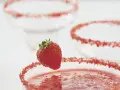 Orzeźwiająca margarita truskawkowa z cukrową posypką na brzegu kieliszka i świeżą truskawką jako dekoracją.