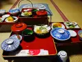 A traditional Japanese meal, perhaps a monk diet, featuring small dishes of tempura, fruit, pickles, and black beans on red lacquer trays.