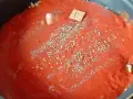 Un coulis de tomates mijote dans une poêle, agrémenté d'herbes et d'un cube de bouillon.