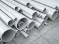 A pile of white pipes, many of which are made of vinyl, a type of plastic, are stacked on a concrete floor.