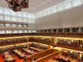Große Bibliothek mit vielen Regalen voller Bücher. Menschen sitzen an Tischen und lesen. Ein Ort für Lesungen in Berlin.