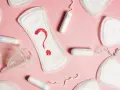 Brązowe plamienie zamiast okresu? Podpaski, tampony i kubeczek menstruacyjny na różowym tle symbolizują niepewność.