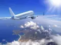 Un aereo bianco solca il cielo azzurro sopra una costa frastagliata. Il sole splende, creando un senso di distacco del vitreo e aereo.