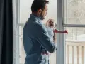 Ojciec trzyma płaczące dziecko przy oknie, gdy matka wychodzi.