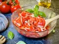 Frischer tomatensalat mit zwiebeln, garniert mit Basilikum. Daneben liegen frische Tomaten und ein Holzlöffel.