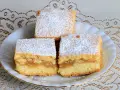 Pyszne ciasto z jabłkami, posypane cukrem pudrem, prezentuje się apetycznie na białym talerzyku.