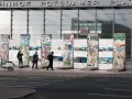 Bunte Reste des Berliner Mauer-Denkmals vor dem Bahnhof Potsdamer Platz. Menschen spazieren vorbei, ein Roller parkt daneben.