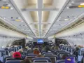 Wnętrze samolotu Boeing 737 Ryanair. Pasażerowie siedzą w rzędach niebieskich foteli, patrząc w stronę kokpitu.