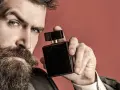 Mężczyzna z brodą trzyma czarne perfumy. Zastanawia się, gdzie psikać perfumy męskie, by zapach był subtelny i uwodzicielski.