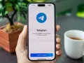Dłoń trzyma smartfon z otwartą aplikacją Telegram. Na ekranie widnieje logo i napis "Telegram. The world's fastest messaging app. It is free and secure.