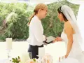 Panna młoda z welonem i wedding plannerka dyskutują przy stole. Czy warto wynająć wedding plannera, czy poradzić sobie samemu?